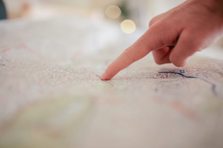 Zdjęcie przedstawia mapę i palec wskazujący na jedno miejsce na mapie.